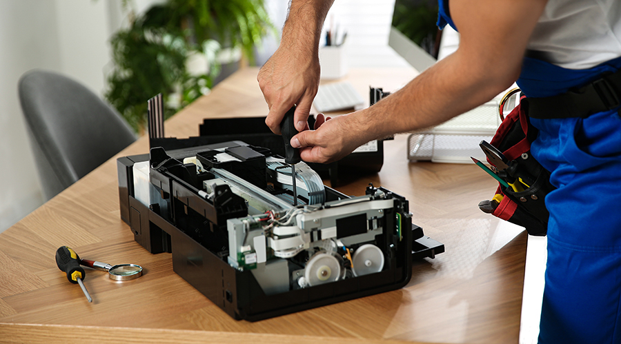 Repairman with screwdriver fixing modern printer indoors, closeup