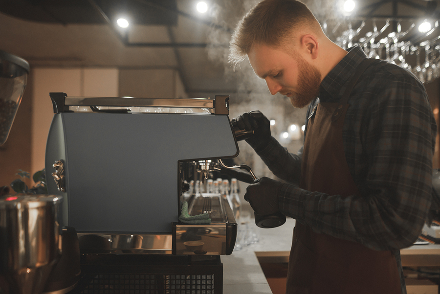 Barista Steaming Milk In Pinscher. Portrait Of Bearded Concentra